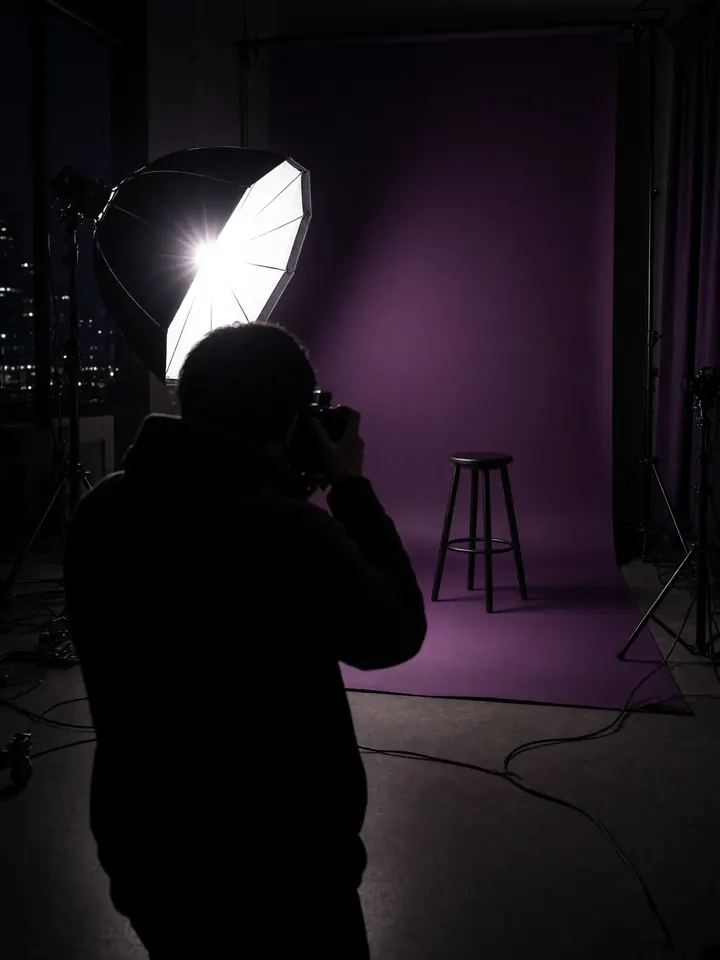 A photographer's flash firing at an empty plum backdrop with a single stool
